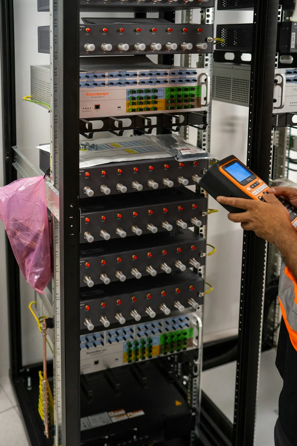 Profissional de TI conferindo equipamentos de um rack de servidores com um leitor portátil.